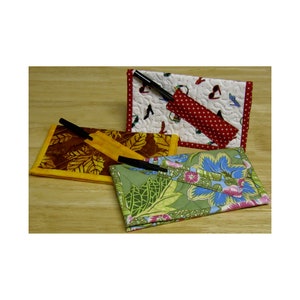 May include: Three fabric pencil holders with different patterns. The first is a red and white polka dot pattern, the second is a brown and yellow leaf pattern, and the third is a green and blue floral pattern.