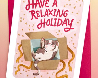 May include: A greeting card with a pink background and a white border. The card features a cartoon cat relaxing in a cardboard box with the text "Have a Relaxing Holiday" in red. Gold stars and ribbons decorate the card.