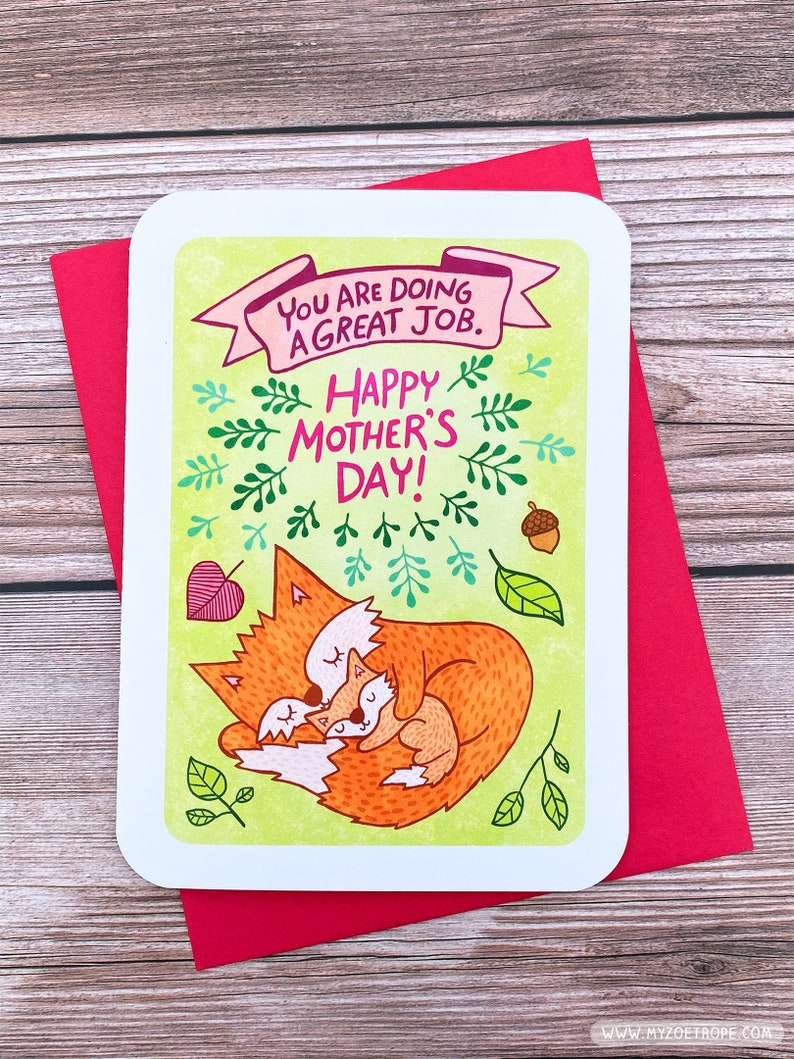 Puede incluir: Una tarjeta de felicitaci&oacute;n con un fondo verde y una pancarta rosa que dice "You are doing a great job." La tarjeta tambi&eacute;n presenta un zorro y un cachorro de zorro acurrucados, rodeados de hojas verdes y bellotas. El texto "Happy Mother's Day!" est&aacute; escrito en letras negras.