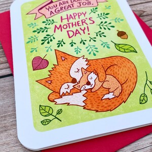 Puede incluir: Una tarjeta verde con un zorro y un cachorro de zorro acurrucados. La tarjeta tiene el texto "You are doing a great job. Happy Mother's Day!" en letras rosas y verdes.