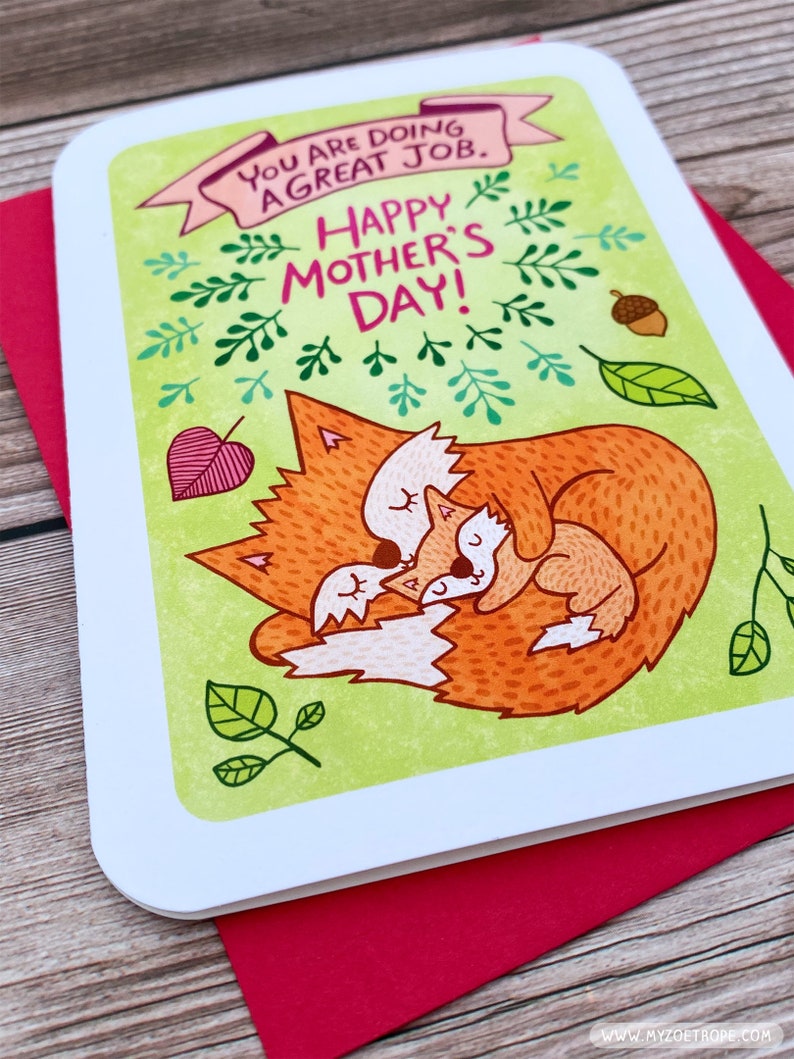 Puede incluir: Una tarjeta verde con un zorro y un cachorro de zorro acurrucados. La tarjeta tiene el texto "You are doing a great job. Happy Mother's Day!" en letras rosas y verdes.