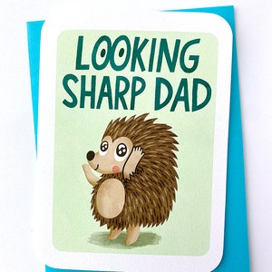 Puede incluir: Una tarjeta de felicitación con fondo verde y borde blanco. La tarjeta presenta un erizo de dibujos animados con ojos grandes y el texto "Looking Sharp Dad".