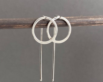 May include: A pair of silver hoop earrings with a thin, straight bar hanging from each hoop.