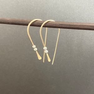 May include: A pair of gold hoop earrings with two small silver beads on each hoop.