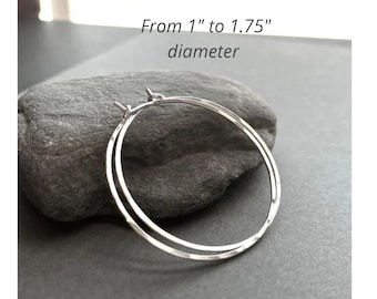 May include: A pair of silver hoop earrings with a thin, circular wire design. The earrings feature a textured surface and have a diameter ranging from 1 inch to 1.75 inches as indicated by the text in the image.