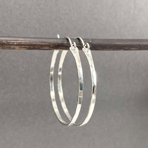 May include: A pair of silver hoop earrings featuring a hammered, textured finish. The circular earrings are constructed from thin, polished metal wire and include a simple hook closure mechanism at the top, designed for standard ear piercings.
