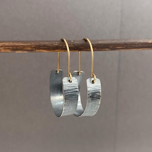May include: A pair of silver hoop earrings with a textured finish and brass hooks.