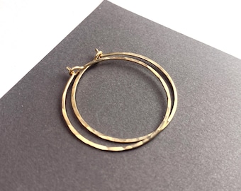May include: A pair of gold hoop earrings featuring a hammered, textured surface. The circular earrings are thin and lightweight, designed with a simple wire closure mechanism that allows the hoops to overlap slightly when resting.