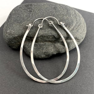 May include: A pair of silver hoop earrings with a hammered finish. The earrings are oval shaped and have a smooth, polished surface.