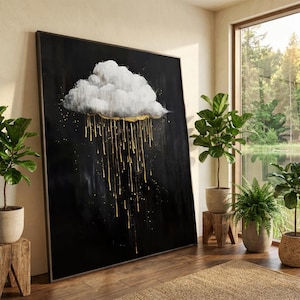 May include: Large framed canvas art depicting a white cloud with gold accents against a black backdrop. Gold drips cascade from the cloud, creating a striking contrast. The artwork is displayed in a well-lit room with plants and a window.