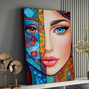 May include: A framed canvas art print depicting a split face. One side has a vibrant eye with orange and red tones, the other a blue eye. The artwork uses geometric patterns and a colourful palette of blues, yellows, and reds. The lips are a bright pink.