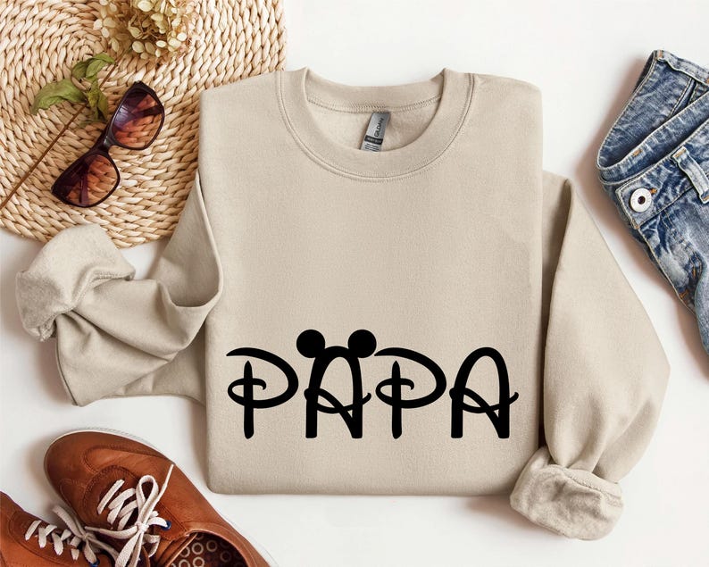 May include: A tan sweatshirt with a black graphic of Mickey Mouse ears and the word "PAPA" in a stylised font.