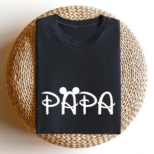 May include: Black t-shirt with a white graphic of Mickey Mouse ears and the word "PAPA" in a stylised font.