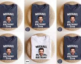 May include: A collection of folded t-shirts, each featuring a personalized design. The shirts are navy blue and white, with the name "Michael" and a photo, along with "20th Birthday Crew" or "My 20th Birthday" printed on them. The shirts are displayed on woven mats.