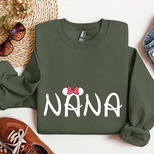 May include: A green sweatshirt with a white graphic of the word "NANA" with a red and white bow on top of the first letter.