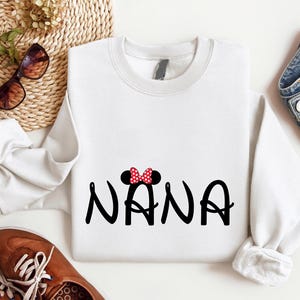 May include: White sweatshirt with a black and red Mickey Mouse inspired design that says "NANA" in a playful font.