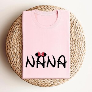 May include: Pink t-shirt with a black and red Mickey Mouse ears design and the word "NANA" in black.