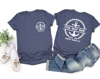 May include: Two navy blue t-shirts with white anchor designs and text. One shirt has the text "YOUR BOAT NAME" and "SINCE: 2000 BOSTON HARBOR, MA". The other shirt has the same text. White sneakers and blue jeans are also in the image.