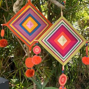 May include: Two colorful dreamcatchers with intricate woven patterns and pom-pom accents hanging from a tree branch.