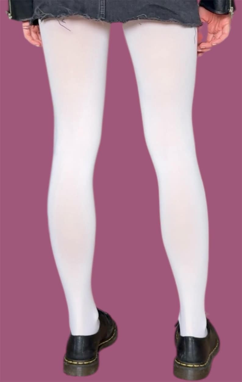 May include: Opaque white tights worn with a dark charcoal gray denim mini skirt featuring a frayed hem and black leather shoes with yellow stitching. The tights provide full coverage from the waist down to the ankles, creating a clean look.