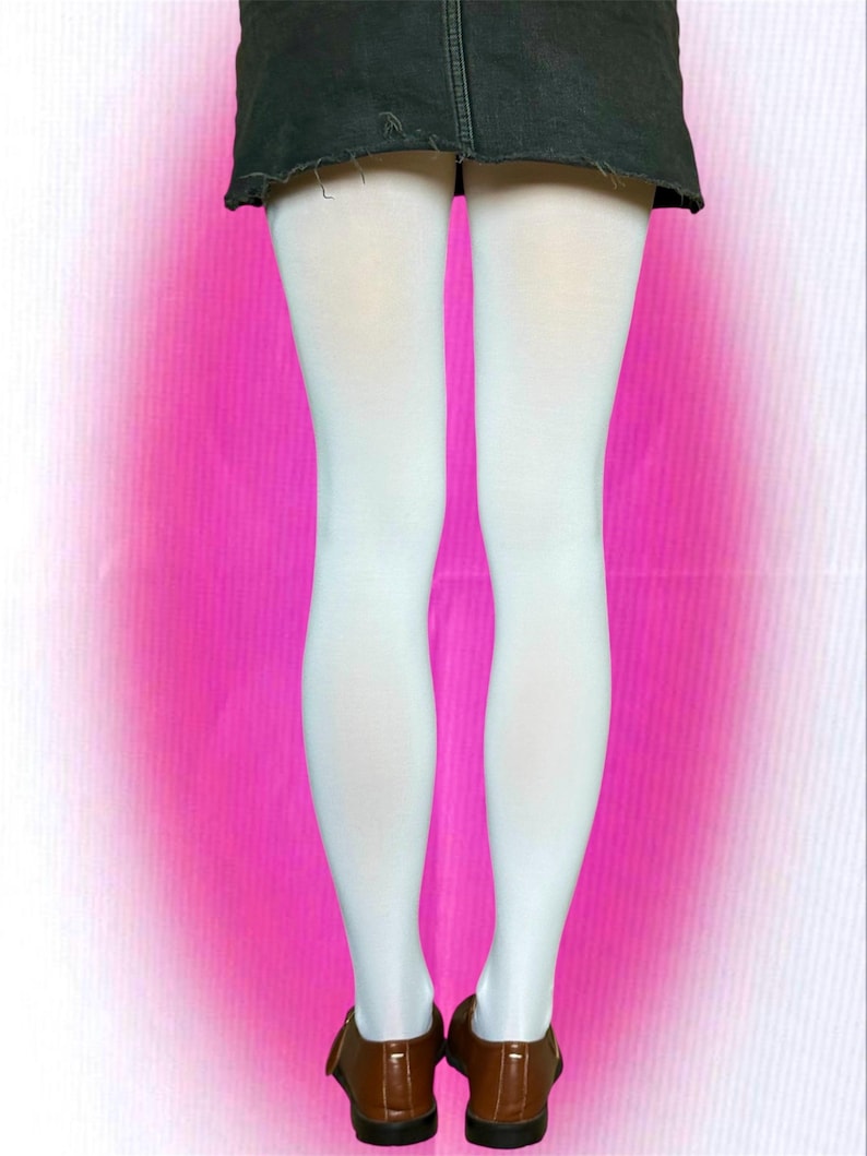 May include: A pair of opaque white tights worn with a dark charcoal gray denim mini skirt featuring a raw, frayed hemline and a pair of brown leather shoes with a rounded toe and a low heel, viewed from the back against a bright pink background.