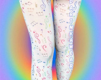 Puede incluir: Medias blancas con un patrón repetitivo de notas y símbolos musicales coloridos en tonos rojo, azul, verde y morado. El texto "DARINKAWEAR" está impreso verticalmente en letras azul claro a lo largo del lado de la pierna derecha.