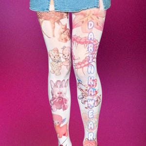 Peut inclure: Collants blancs ornés d'un collage d'illustrations roses et brunes représentant un faon, des ours en peluche, un mille-pattes, un caniche et une fraise. Le texte DARINKAWEAR est imprimé verticalement en bleu sur la jambe droite sous une jupe en jean.