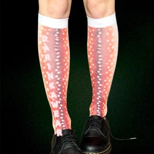 May include: Knee-high socks with a red and white spotted design, and the word "DARKWEAR" in white. The socks are worn with black leather shoes. The background is dark green.