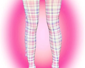 Puede incluir: Leggings con un patrón de cuadros en rosa, blanco y morado con el texto vertical "DARINKAWEAR" impreso en azul claro en la pierna derecha, combinados con una minifalda de mezclilla oscura y zapatos de cuero negro con cordones y costuras amarillas.