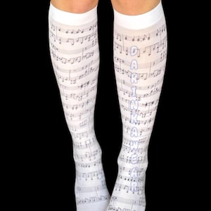 Könnte beinhalten: Weiße Kniestrümpfe mit einem Notenmuster. Die Socken zeigen ein sich wiederholendes Muster aus Noten und Notenlinien. Das Wort "DARINKAWEAR" ist vertikal auf die Seite einer Socke gedruckt.