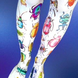 May include: White leggings featuring a vibrant, multi-colored print of various beetle species in shades of red, blue, green, yellow, and purple. The text DARINKAWAR is printed vertically in light blue letters along the right leg of the garment.