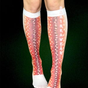 May include: Knee-high socks featuring a deer-like pattern in red, purple, and white. The socks have white cuffs and foot sections. The word "DRINKAWEAR" is printed vertically on the side of the socks.