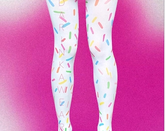 Puede incluir: Medias blancas con un patrón de chispas de colores en tonos rosa, azul, amarillo y verde. El texto DARINKAWEAR está impreso verticalmente en una fuente fina y clara a lo largo de la pierna derecha. Las medias se combinan con una falda negra plisada.