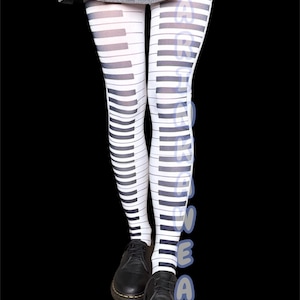 Puede incluir: Medias blancas y negras con estampado de teclas de piano. Las medias presentan un diseño repetido de teclas de piano, con teclas negras sobre un fondo blanco. La persona lleva zapatos negros y una falda gris. La palabra "DANCEWEAR" está impresa verticalmente.