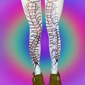 May include: White tights featuring a large, detailed centipede design in brown ink. The text "DARKNKAWEAR" is printed vertically in blue. The tights are paired with brown suede shoes with a buckle.