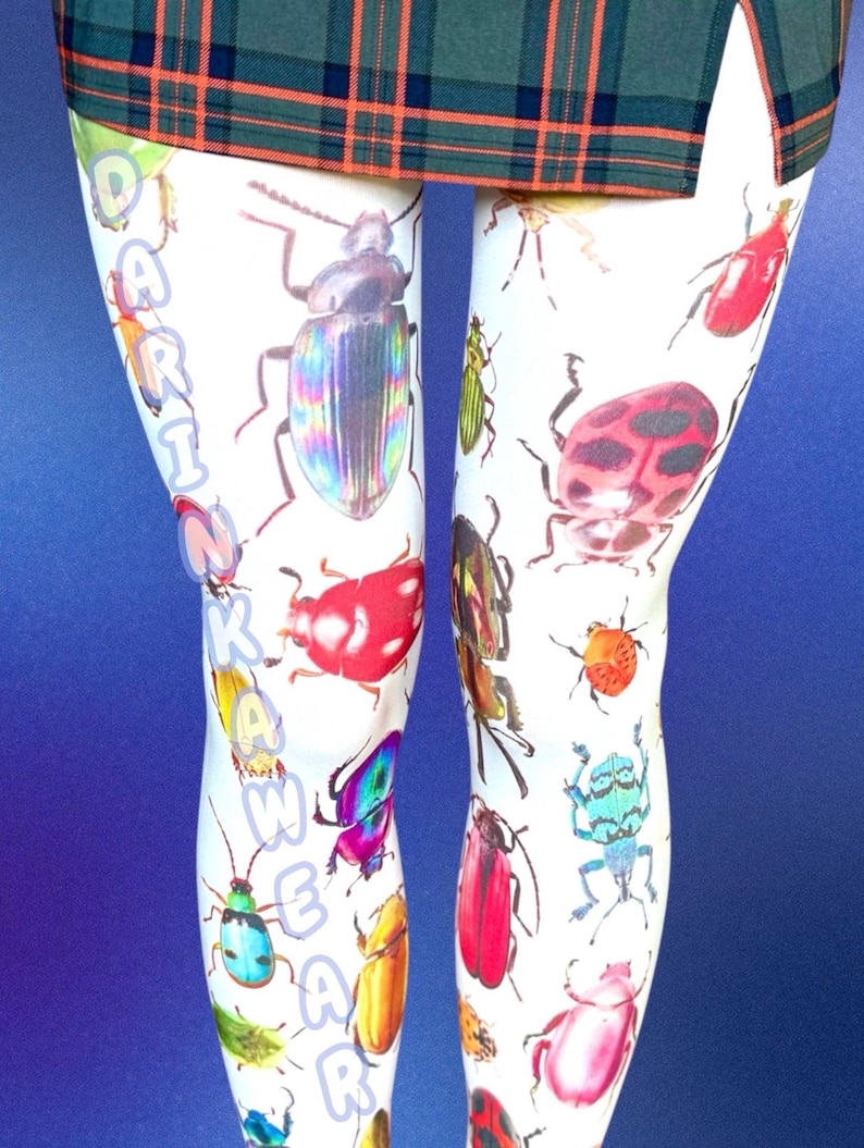 May include: White leggings featuring a colorful all-over print of various beetles and insects in shades of red, blue, green, and yellow. The text DARINKAWEAR is printed vertically in light blue along the left leg. A green plaid skirt is visible at the top.