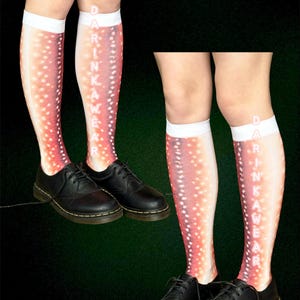 May include: Knee-high socks with a salmon-coloured pattern and white polka dots. The socks feature the text "DRINKAWEAR" printed vertically. Black leather shoes are worn with the socks.