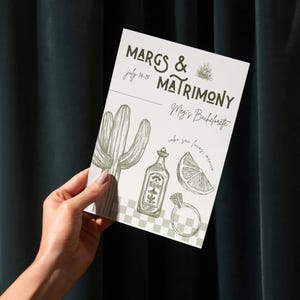 K&ouml;nnte beinhalten: Eine wei&szlig;e Karte mit dem Text "Margs & Matrimony" und "Meg's Bachelorette" in schwarzer Schrift. Die Karte zeigt au&szlig;erdem einen Kaktus, eine Flasche Tequila, eine Limettenscheibe und einen Ring. Die Karte wird in einer Hand vor einem dunkelgr&uuml;nen Hintergrund gehalten.