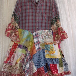 May include: A patchwork dress featuring a red and black plaid button-down shirt bodice. The skirt is a colorful patchwork of various fabrics, including floral, plaid, and polka dot patterns. The sleeves have ruffled floral cuffs.