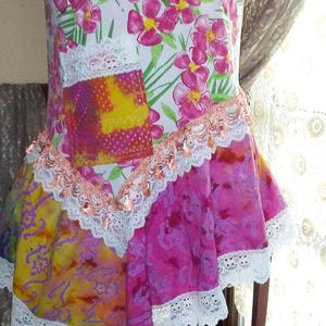May include: A white, pink, and yellow floral print top with a white lace trim and a pink and purple tie-dye fabric panel. The top has a relaxed fit and a flowy silhouette.