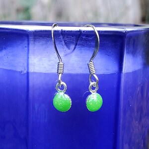 May include: A pair of silver dangle earrings with green glitter round beads.