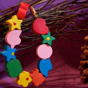 May include: A colorful wooden bead necklace with a heart, star, flower, and leaf shapes. The beads are strung on a red cord and have a gold metal clasp.