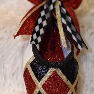 May include: A red and black glittery ballet slipper with a gold trim and a red and black checkered bow.