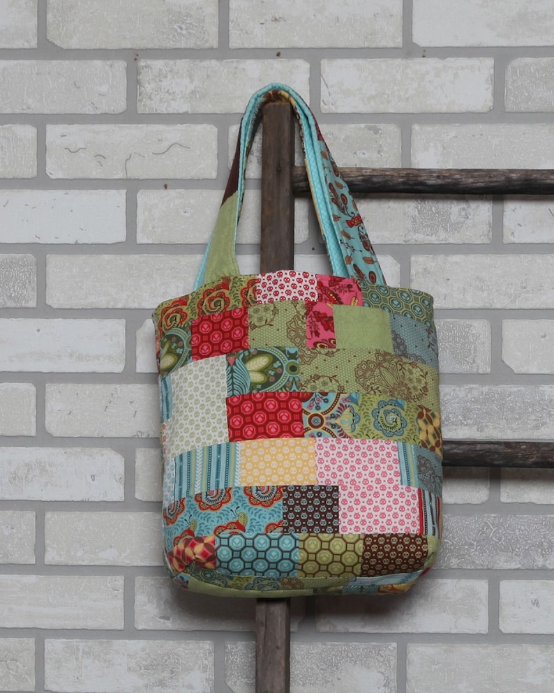 K&ouml;nnte beinhalten: Eine Patchwork-Tragetasche aus verschiedenen bunten Stoffen, darunter Rot, Gr&uuml;n, Blau, Gelb und Braun. Die Tasche hat eine rechteckige Form und zwei Henkel.