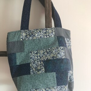 K&ouml;nnte beinhalten: Eine blaue und gr&uuml;ne Patchwork-Tragetasche mit Blumenmuster. Die Tasche hat zwei Henkel und ist aus Stoff.