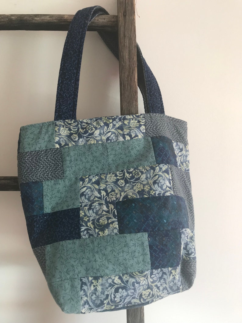K&ouml;nnte beinhalten: Eine blaue und gr&uuml;ne Patchwork-Tragetasche mit Blumenmuster. Die Tasche hat zwei Henkel und ist aus Stoff.