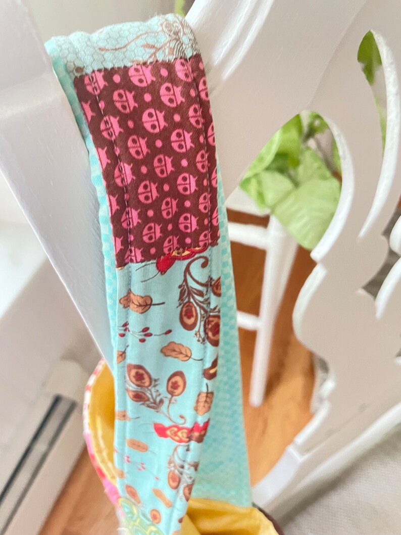 K&ouml;nnte beinhalten: Nahaufnahme einer blauen und braunen Stofftasche mit Patchwork-Muster. Die Tasche hat einen Riemen mit einem Muster aus rosa Marienk&auml;fern auf braunem Hintergrund.