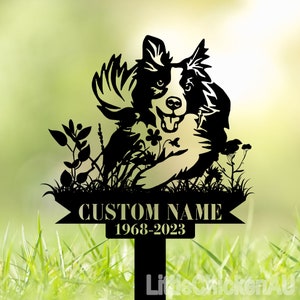 May include: Black metal silhouette of a border collie dog with a playful expression, surrounded by flowers and grass. The sign reads "CUSTOM NAME 1968-2023".