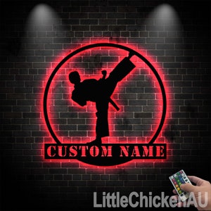 May include: Red neon sign with a silhouette of a martial arts figure in a kicking pose. The sign has a circle around the figure and the words "CUSTOM NAME" below the circle.