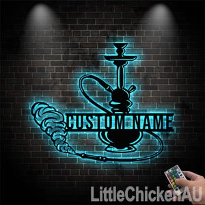 May include: A black metal silhouette of a shisha with a custom name plate. The silhouette is lit with blue neon lights against a brick wall background.